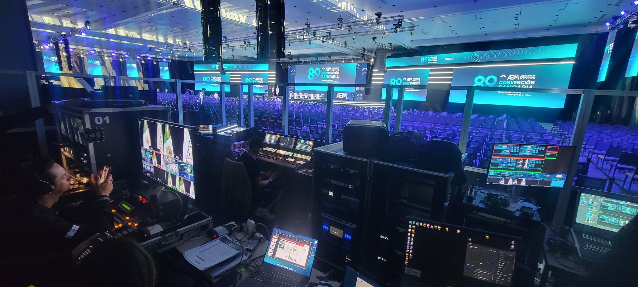Cabina de control de video con monitores y switcher frente a una arena con pantallas LED en la Convención Bancaria